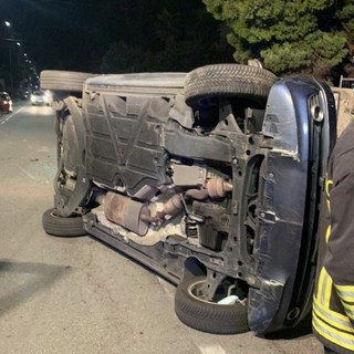 Va a sbattere contro un'auto parcheggiata e si ribalta