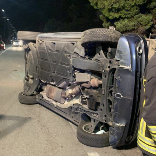 Va a sbattere contro un'auto parcheggiata e si ribalta