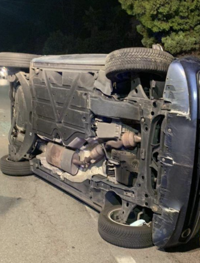 Va a sbattere contro un'auto parcheggiata e si ribalta