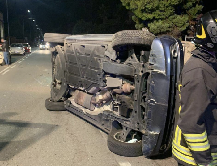 Va a sbattere contro un'auto parcheggiata e si ribalta